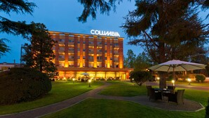 Een hotel met een 'COLUMBIA' bord, een verzorgd gazon en terrasplekken.