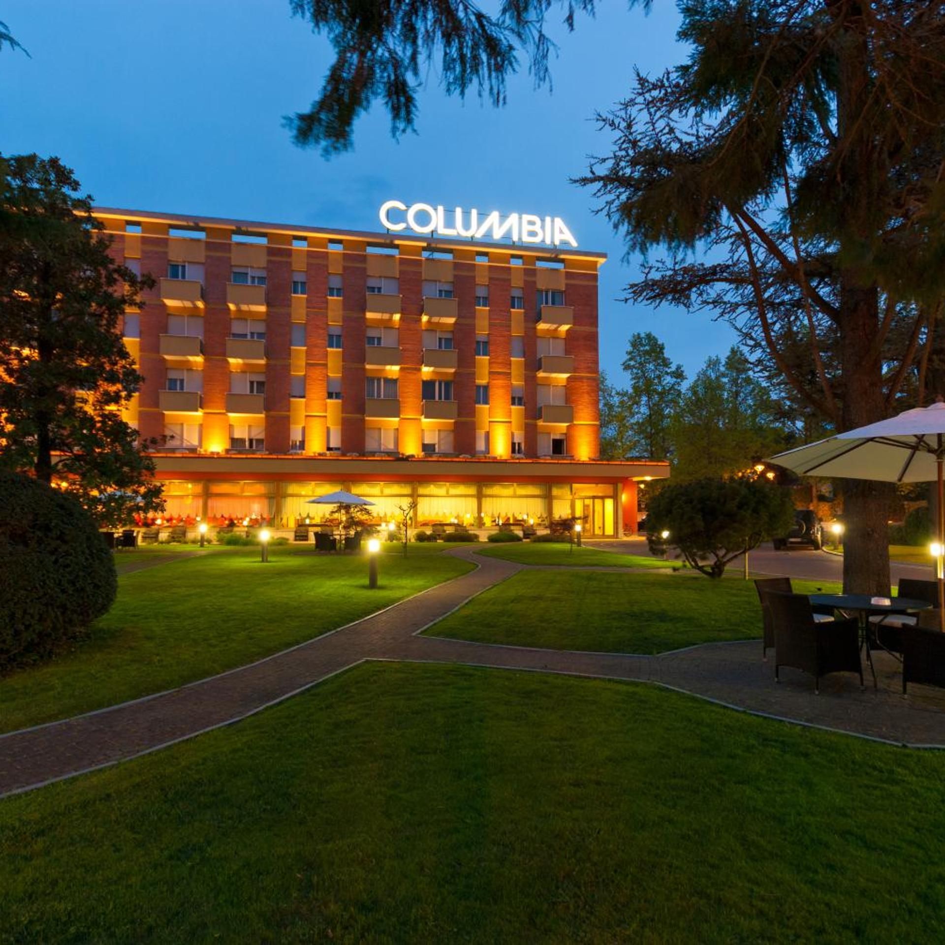 A multi-story hotel with a prominent 'COLUMBIA' sign, a well-maintained lawn, and outdoor seating area.
