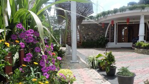 A courtyard with a stone pathway, potted plants, and a building entrance with a wooden door. - White Tower Villa  Sri Lanaka (Nuwara Eliya)