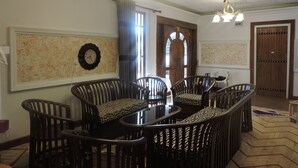 A dining area with a round table surrounded by wooden chairs with patterned cushions, a wall clock, and a ceiling with a floral pattern. - White Tower Villa  Sri Lanaka (Nuwara Eliya)