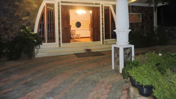 A stone building with a porch, a wooden door, and a circular window. - White Tower Villa  Sri Lanaka (Nuwara Eliya)