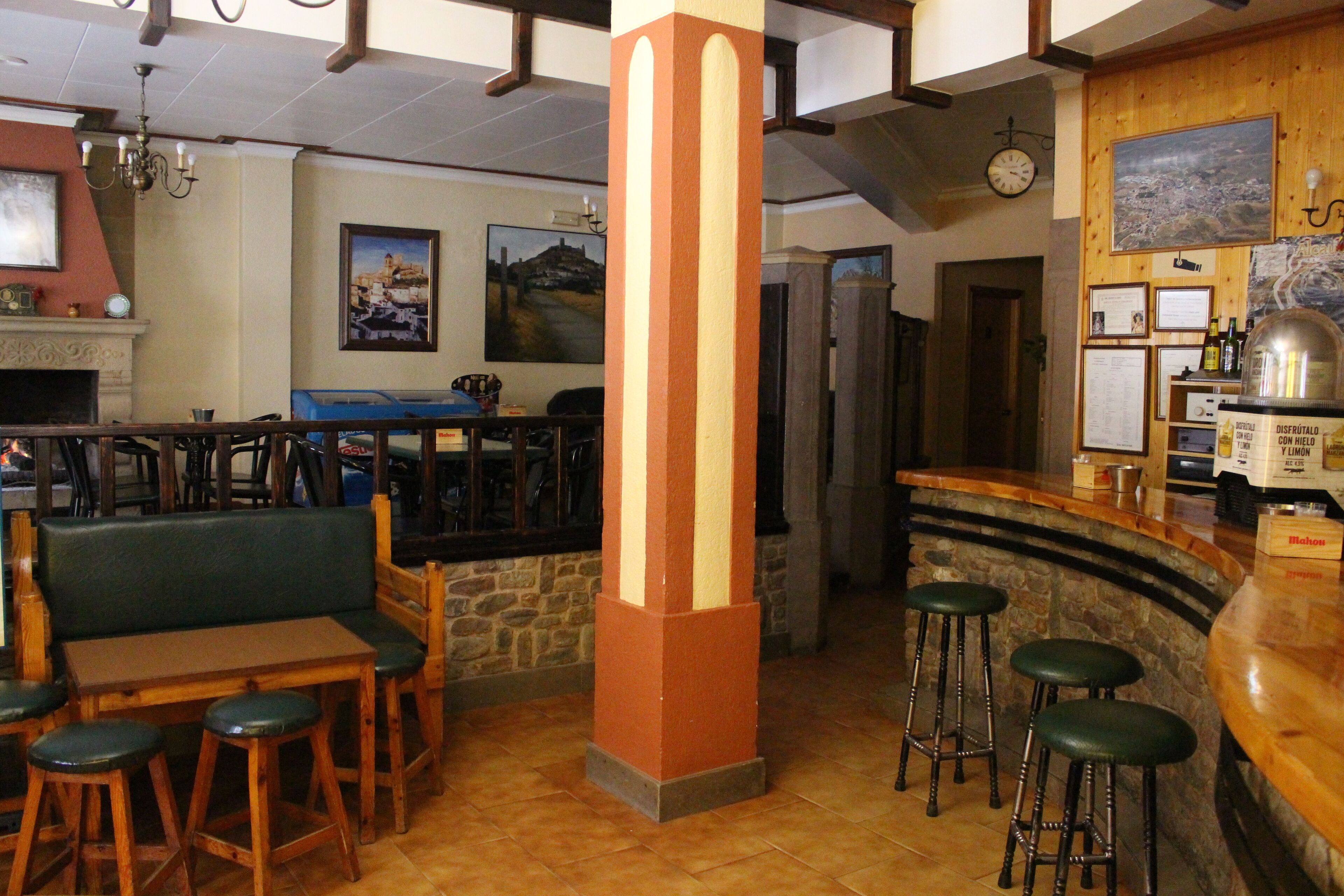 A restaurant interior with wooden furniture, a stone column, a bar area, and a clock on the wall.