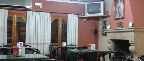A dining area with tables and chairs, a television mounted on the wall, and a fireplace.