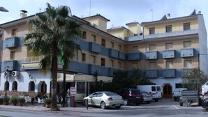 Un hotel de varios pisos con balcones, zona de estacionamiento y mobiliario exterior.