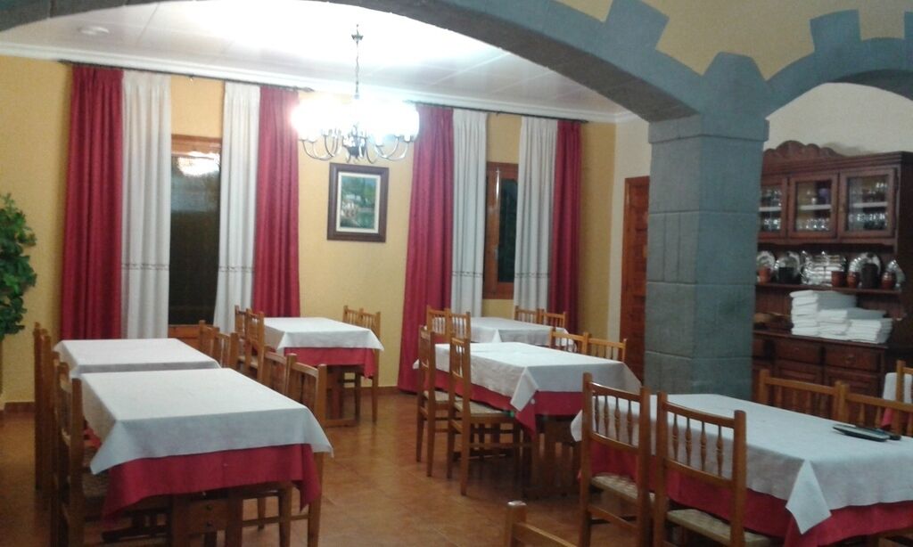 Comedor con varias mesas y sillas, un candelabro y un mueble de madera con cristalería.