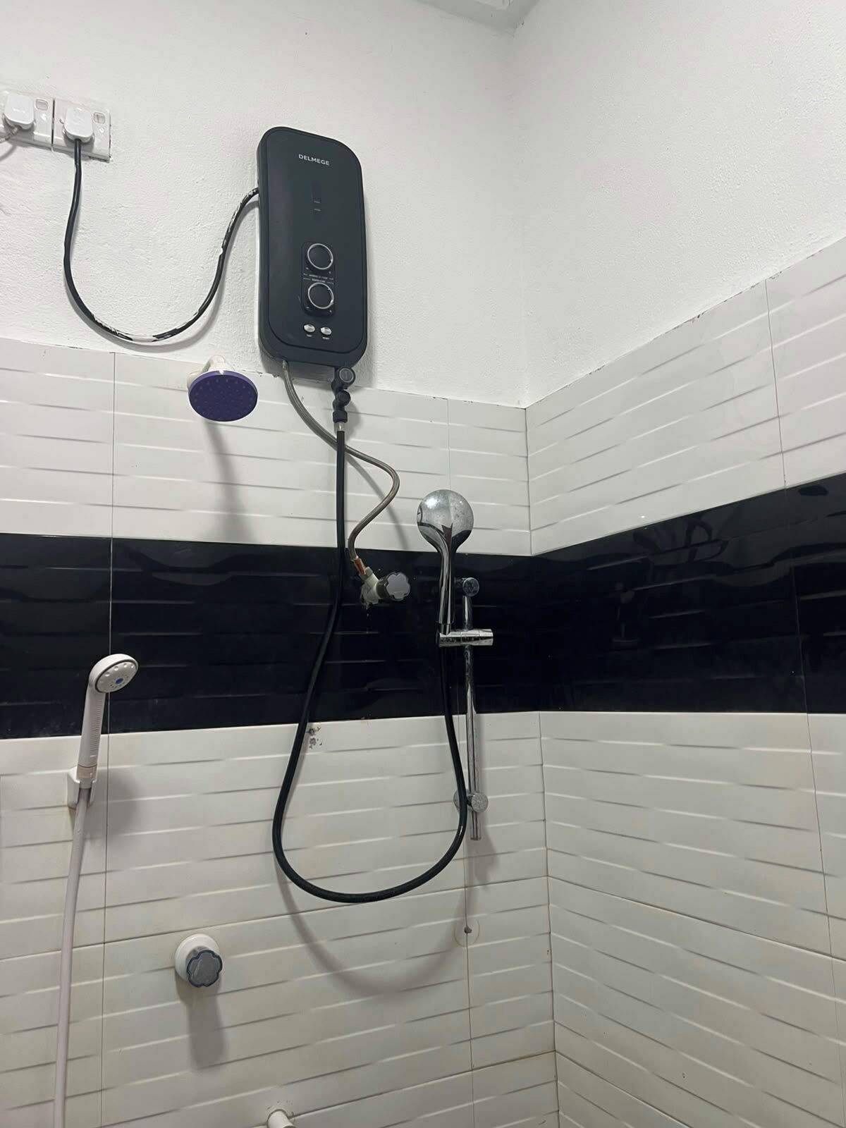 A bathroom with a black and white tiled wall, a handheld showerhead, a wall-mounted faucet, and a control panel.