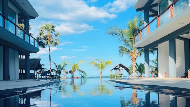 A modern resort with a clear pool, palm trees, and a view of the ocean.