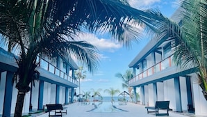 A modern hotel with a pool, palm trees, and a clear sky.