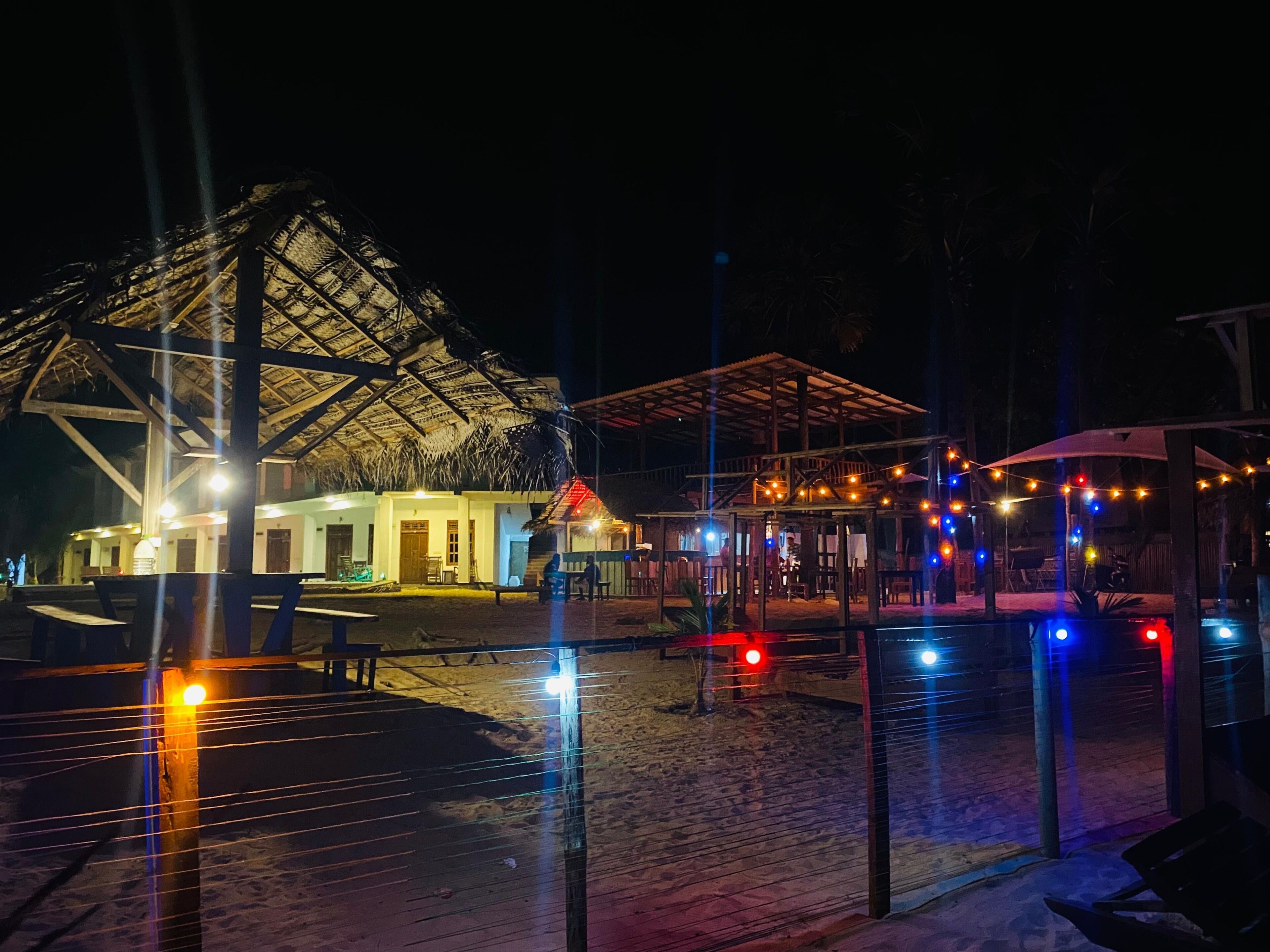 Un resort frente a la playa con una estructura de techo de paja, asientos al aire libre y luces colgantes.
