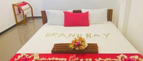Une chambre d’hôtel avec un lit, une couvre-lit rouge et blanche, un oreiller rouge et un arrangement floral sur le lit.