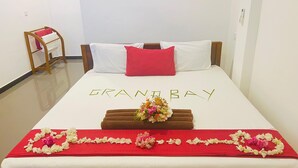 A hotel room with a bed, a red pillow, a bouquet of flowers, and a red and white bedspread.