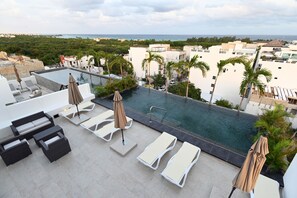 A rooftop pool area with lounge chairs and umbrellas, surrounded by palm trees and buildings.