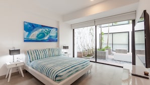 A modern bedroom with a large bed, a painting, a nightstand, and a view of the outdoors through a sliding door. - Icono 107 (Playa del Carmen)