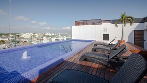 A rooftop pool with a view of the city, lounge chairs, and a palm tree. - Icono 405 (Playa del Carmen)
