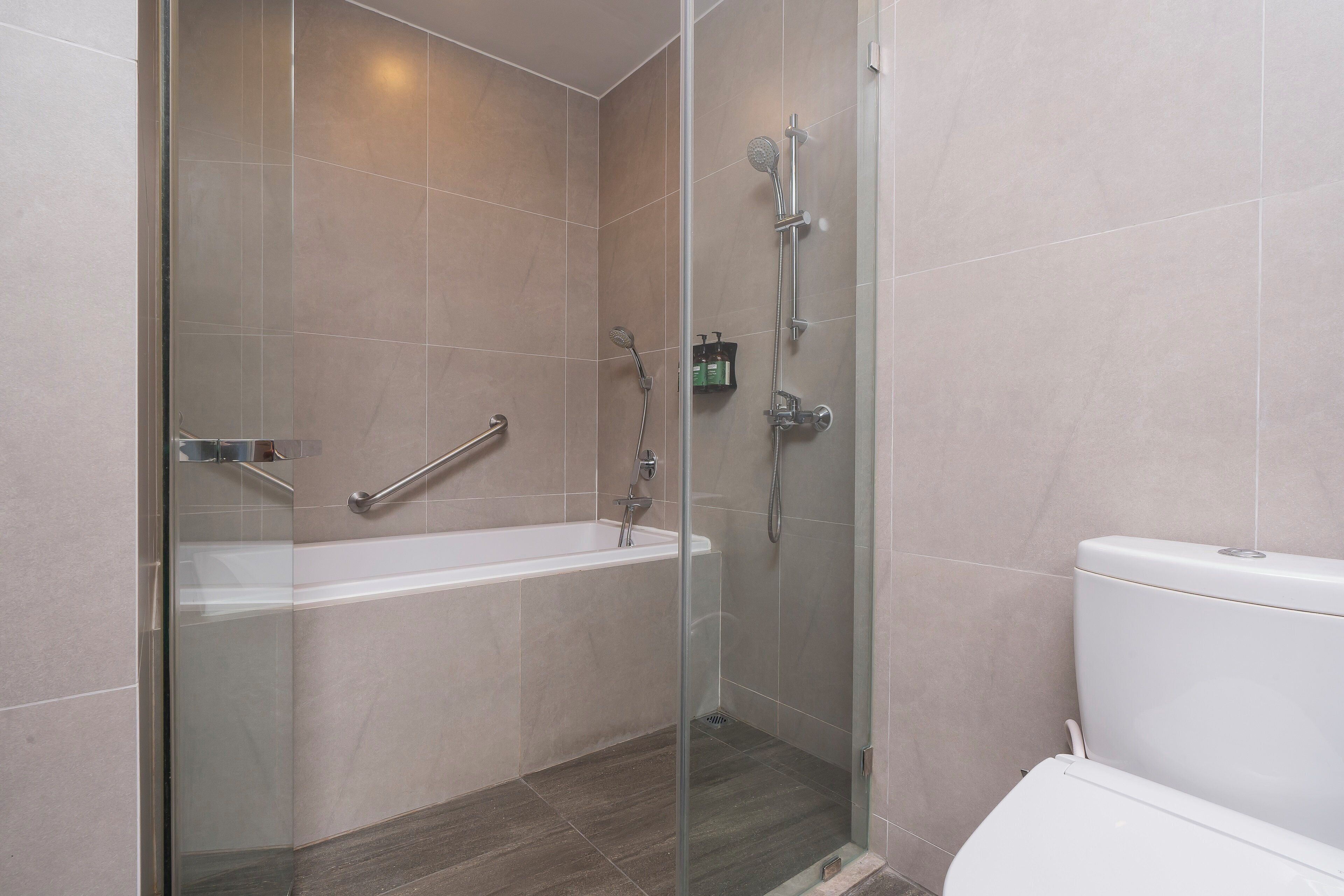 A modern bathroom with a glass-enclosed shower, a white bathtub, and a toilet.