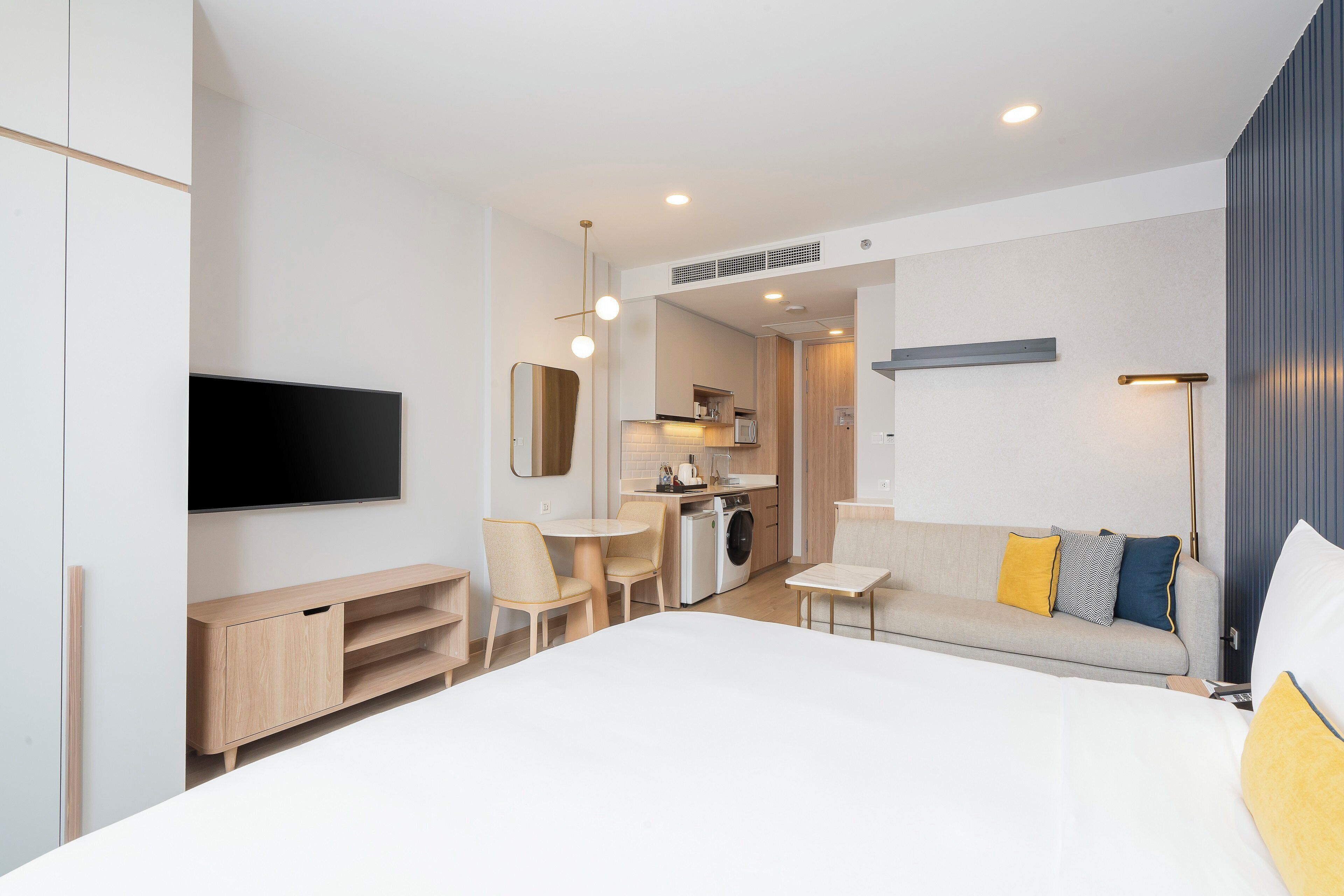 Una habitación de hotel moderna con cama, televisión, kitchenette y mesa de comedor.
