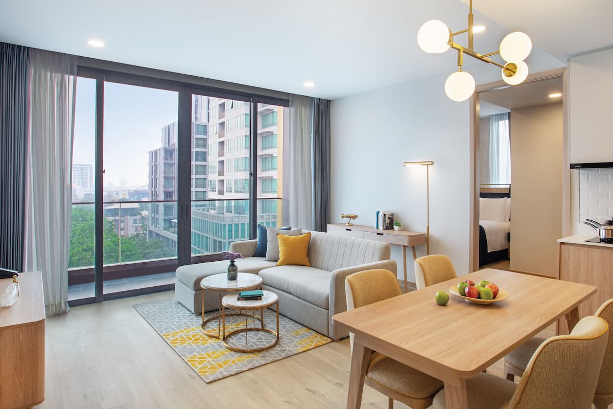 Une chambre d’hôtel moderne dotée d’une grande fenêtre, d’un coin repas, d’une kitchenette et d’un espace de vie comprenant un canapé et une table basse.
