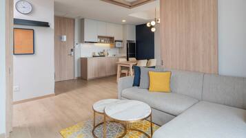 A modern living room with a sofa, two round tables, a kitchen in the background, and a clock on the wall.