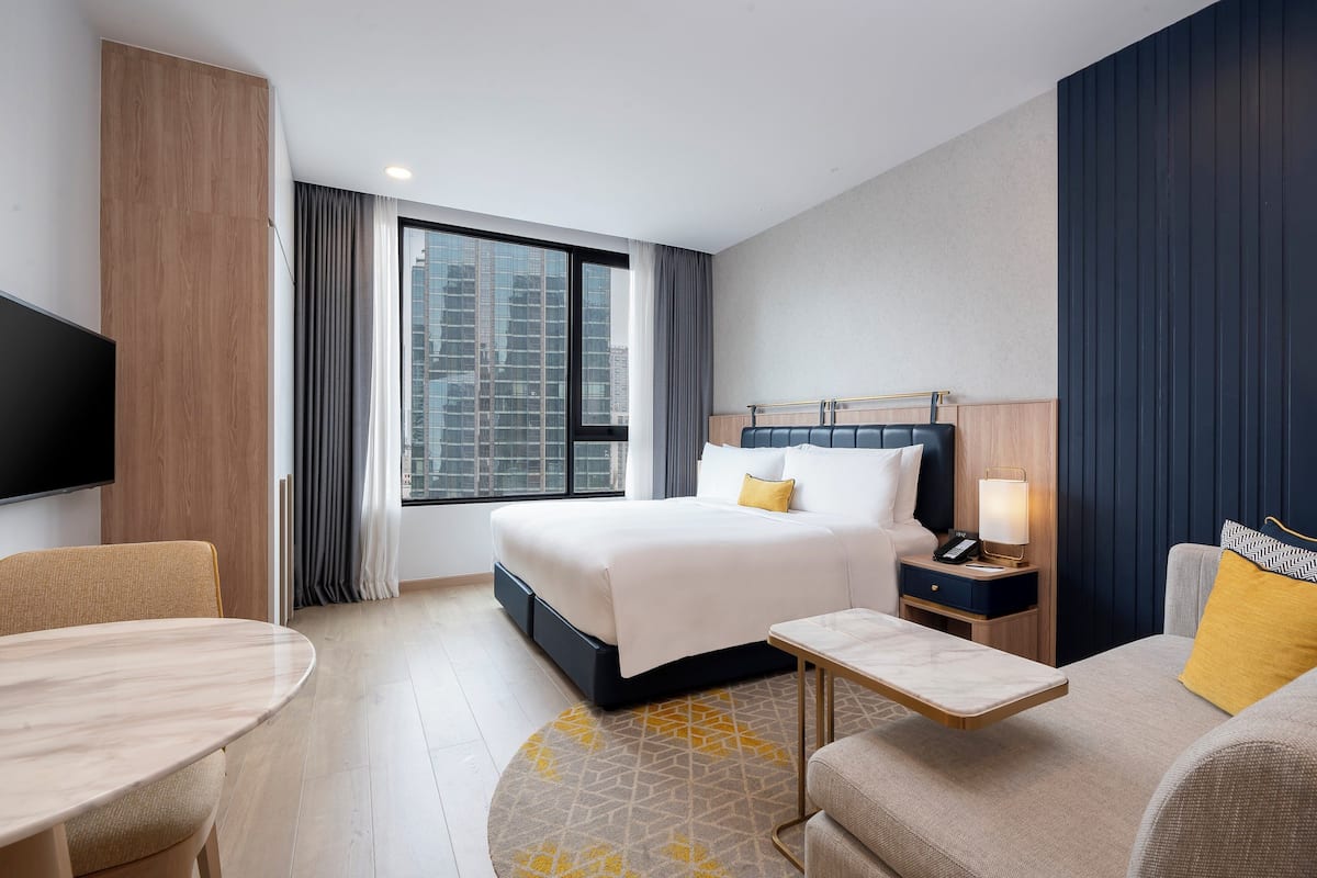 Une chambre d’hôtel équipée d’un lit, d’une table de chevet, d’une lampe, d’une télévision et offrant une vue sur le paysage urbain.
