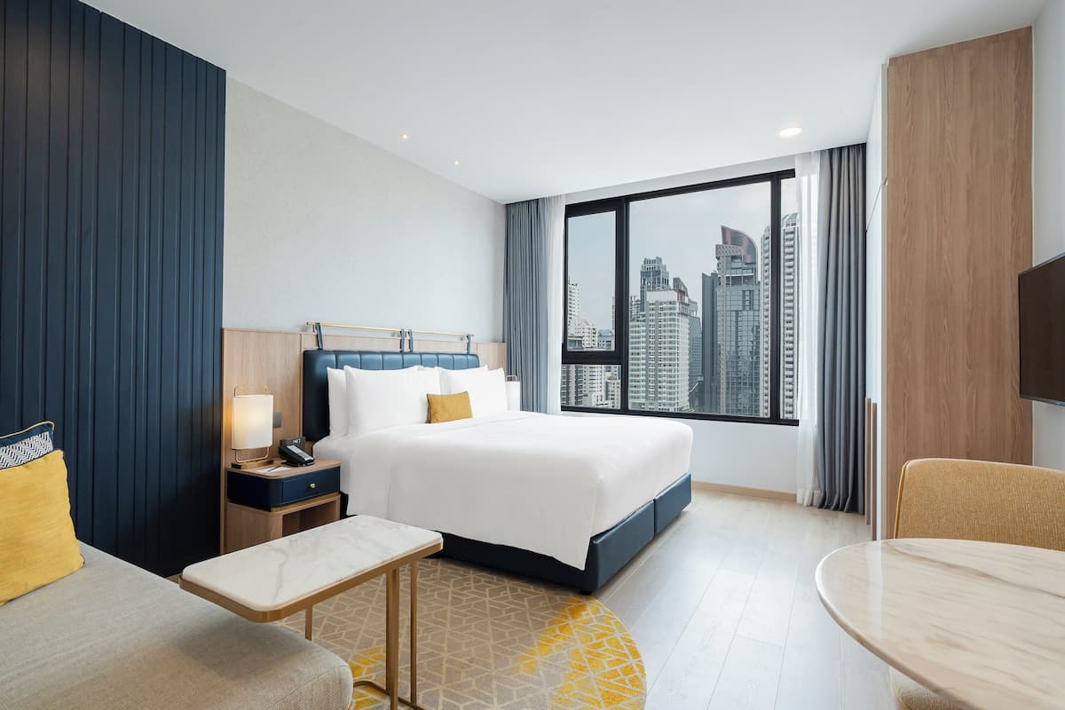 Une chambre d’hôtel avec un grand lit, un bureau, une chaise et une vue sur le panorama urbain.
