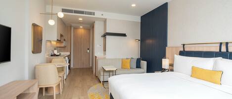 A modern hotel room with a large bed, a desk, a sofa, and a TV.