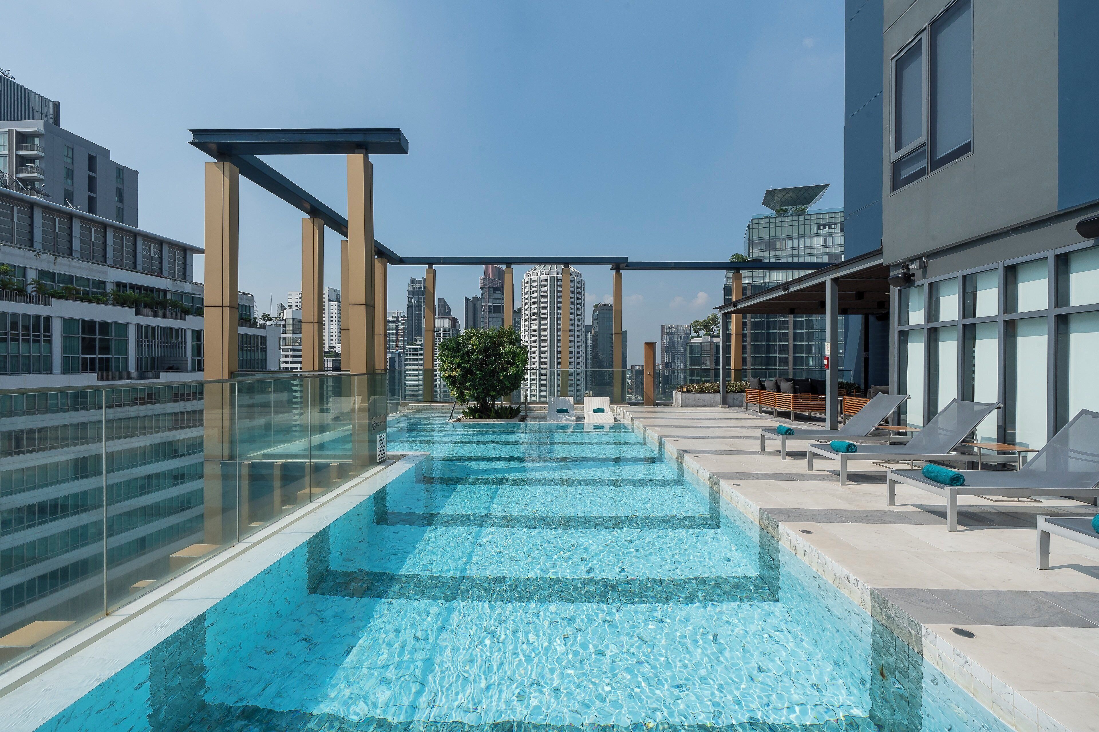 Una piscina sul tetto con acqua cristallina, circondata da sedie a sdraio e una ringhiera in vetro.