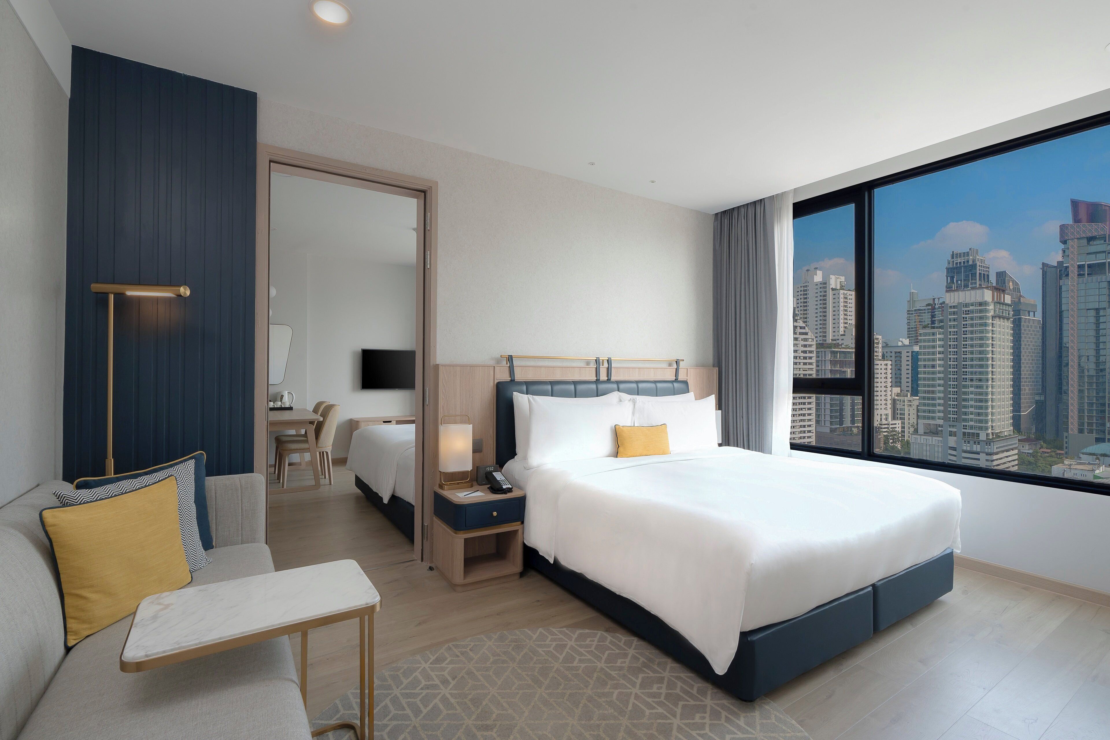 A modern hotel room with a large bed, a seating area, and a city view.