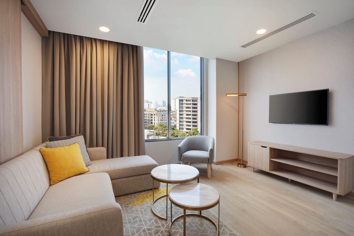 Un salon moderne avec un canapé, un fauteuil, une petite table et un téléviseur fixé au mur.