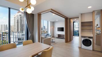 A modern apartment with a dining area, a living room with a TV, a kitchen, and a balcony with a city view.