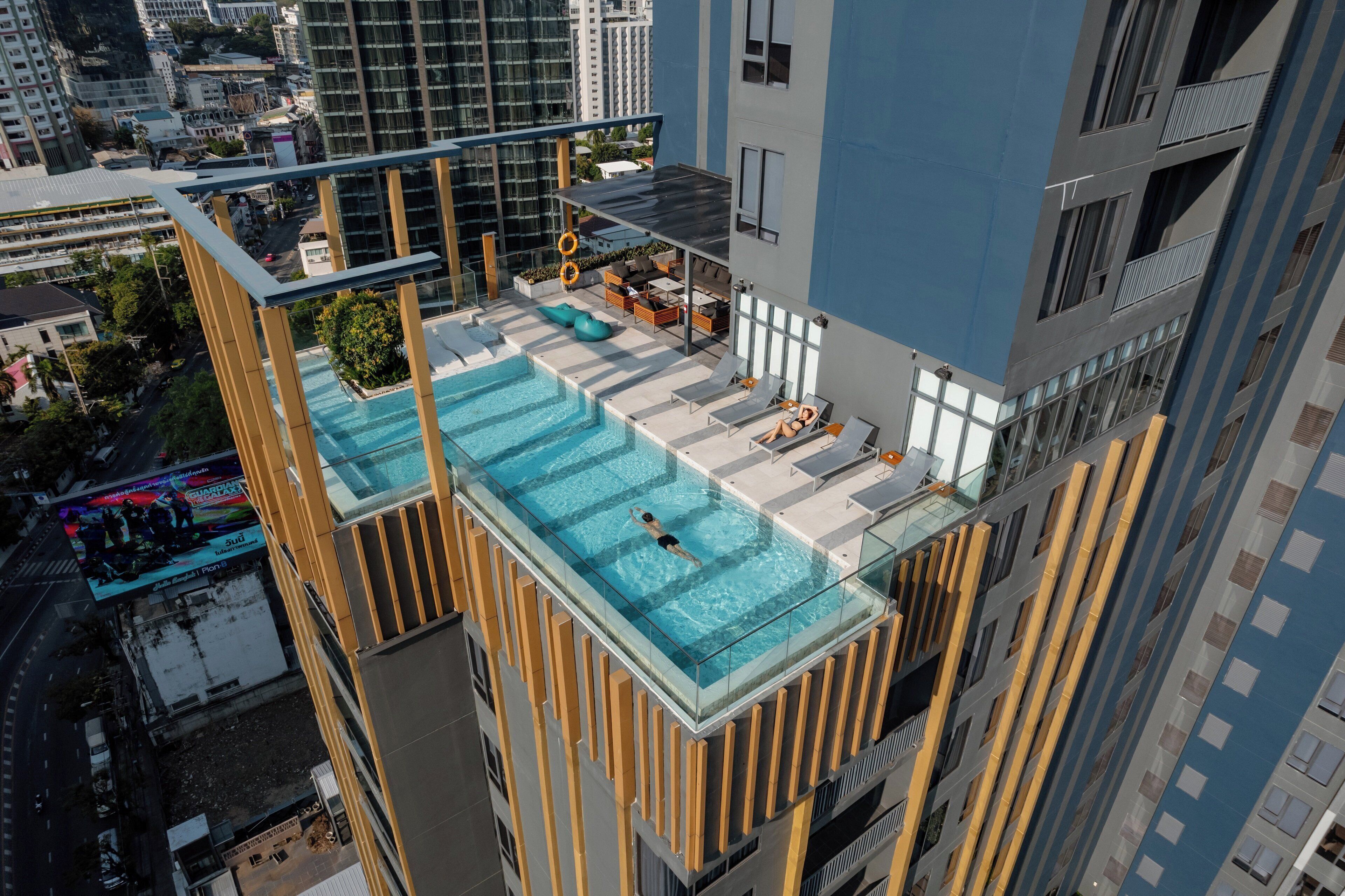 A rooftop infinity pool with a glass barrier, surrounded by outdoor seating and a cityscape view.