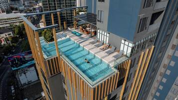 A rooftop infinity pool with a glass barrier, surrounded by outdoor seating and a cityscape view.