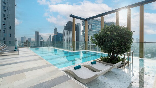 Piscina infinita en la azotea con sillones de descanso, barandilla de vidrio y vista al horizonte de la ciudad.