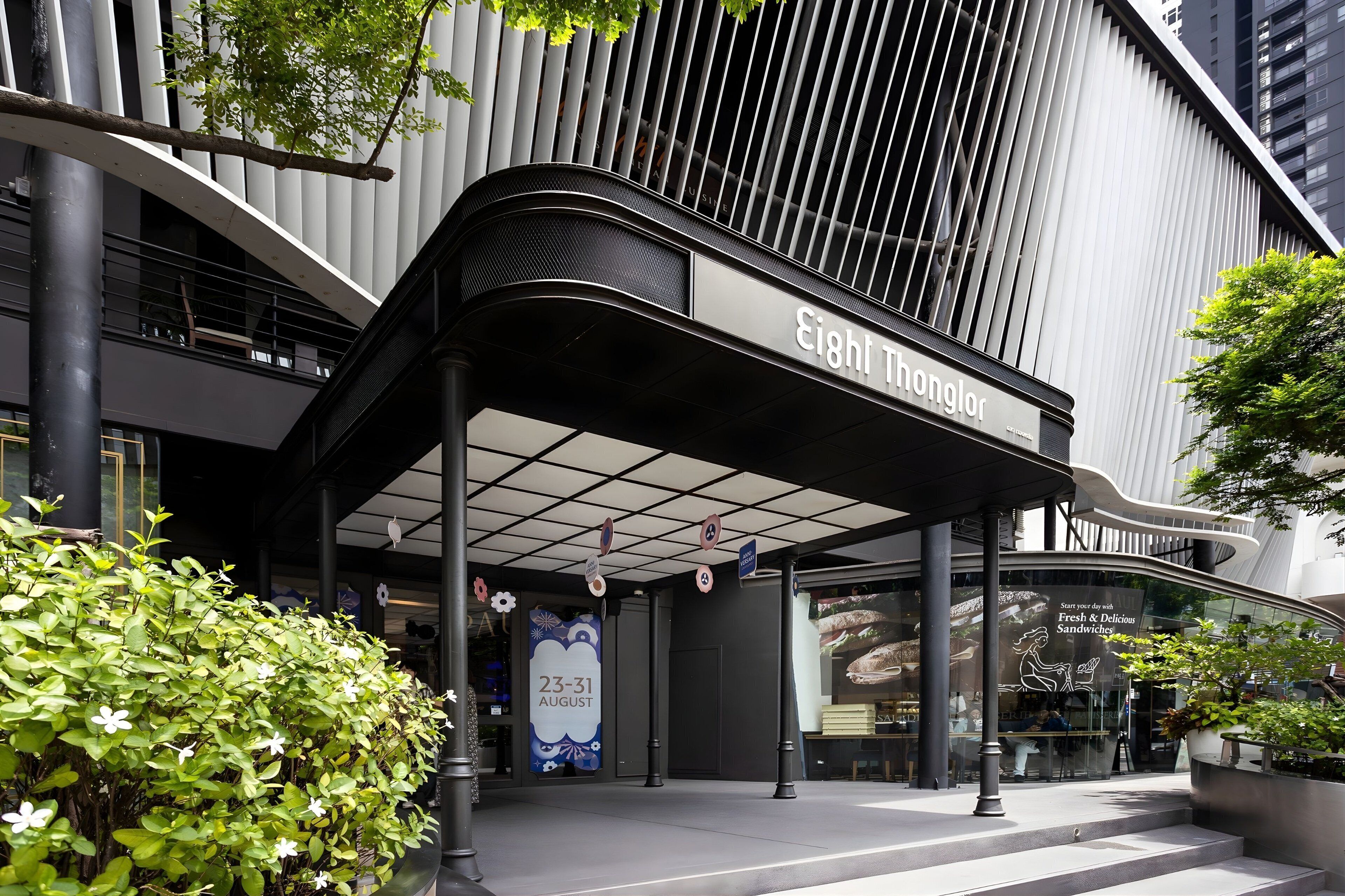 A modern building with a curved entrance and a sign reading "Eight Thonglor".