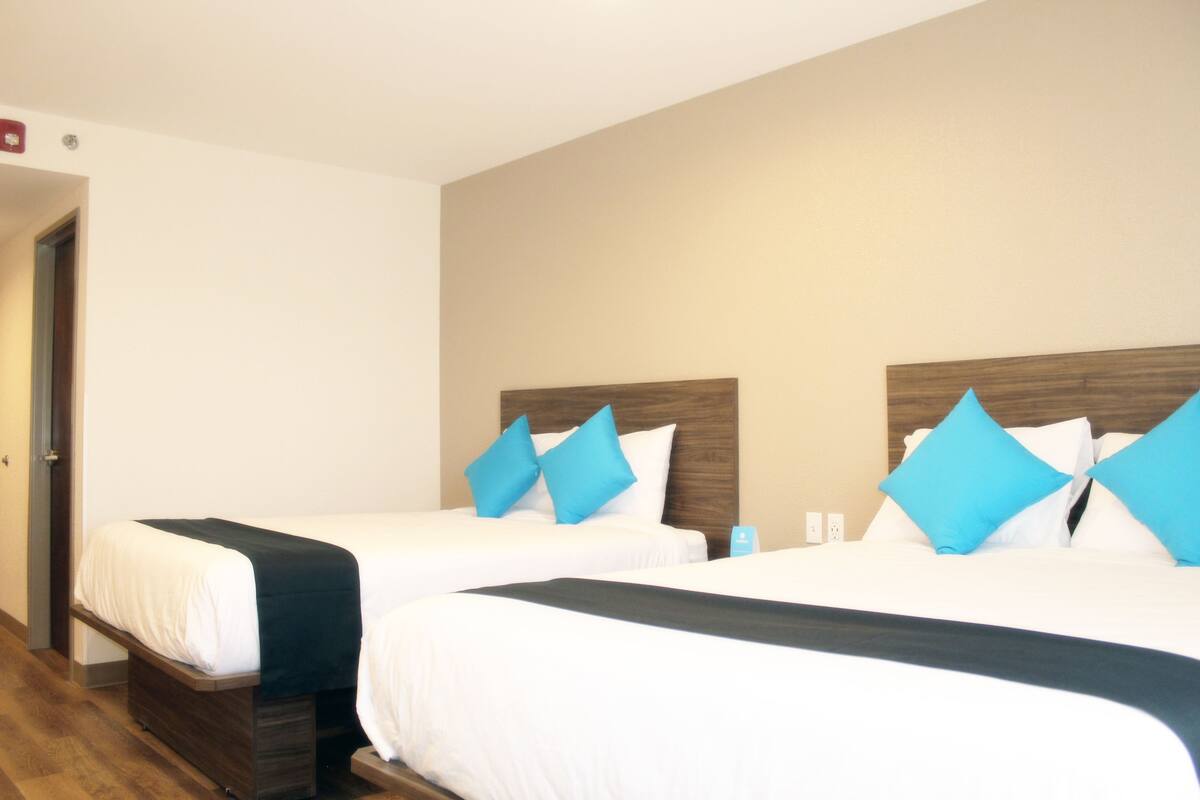 A hotel room with two beds, each with white bedding and blue pillows, and a wooden headboard.