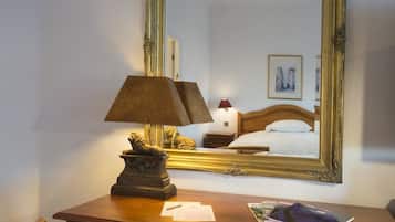 Una camera d'albergo con un letto, una scrivania con una lampada, uno specchio e un quadro appeso al muro.