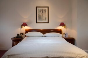 A neatly made bed with white linens, two bedside lamps, a framed artwork above the bed, and a bedside telephone on the left nightstand.