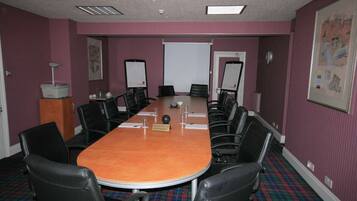 A conference room with a long table, black chairs, a projector screen, and a whiteboard.