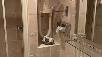 A bathroom with a glass shower enclosure, a sink with a chrome faucet, and a mirror with two wall-mounted lights.