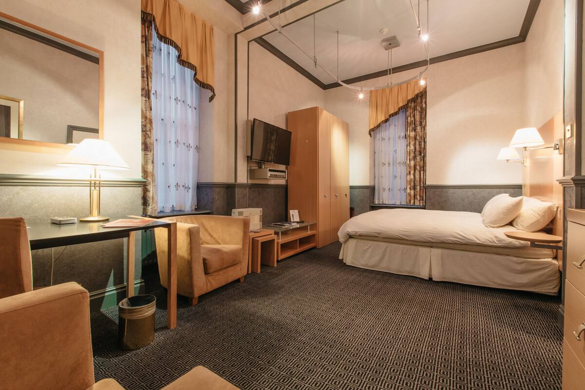 A hotel room with a bed, desk, chair, television, wardrobe, and a small table.