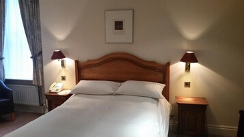 Una cama bien hecha con sábanas blancas, dos lámparas de noche, un cuadro en la pared y un teléfono en la mesita.