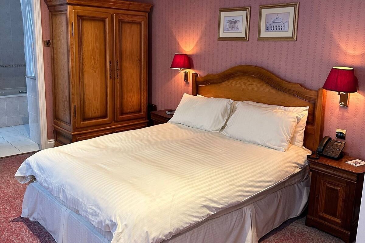A neatly made bed with white linens, a wooden headboard, and two bedside lamps.