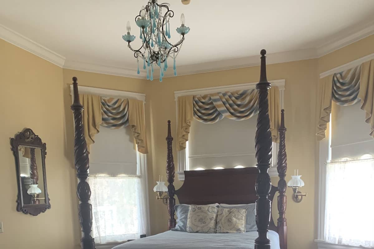 A four-poster bed with a wooden headboard and footboard, a matching bench, and a patterned area rug.