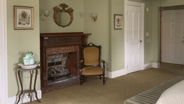 A room with a fireplace, a wooden chair, a bed, and a television mounted on the wall.