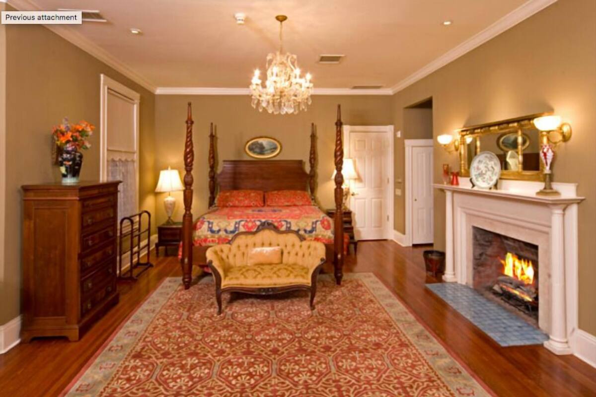 A traditional bedroom with a large bed, a chandelier, a fireplace, and a wooden dresser.