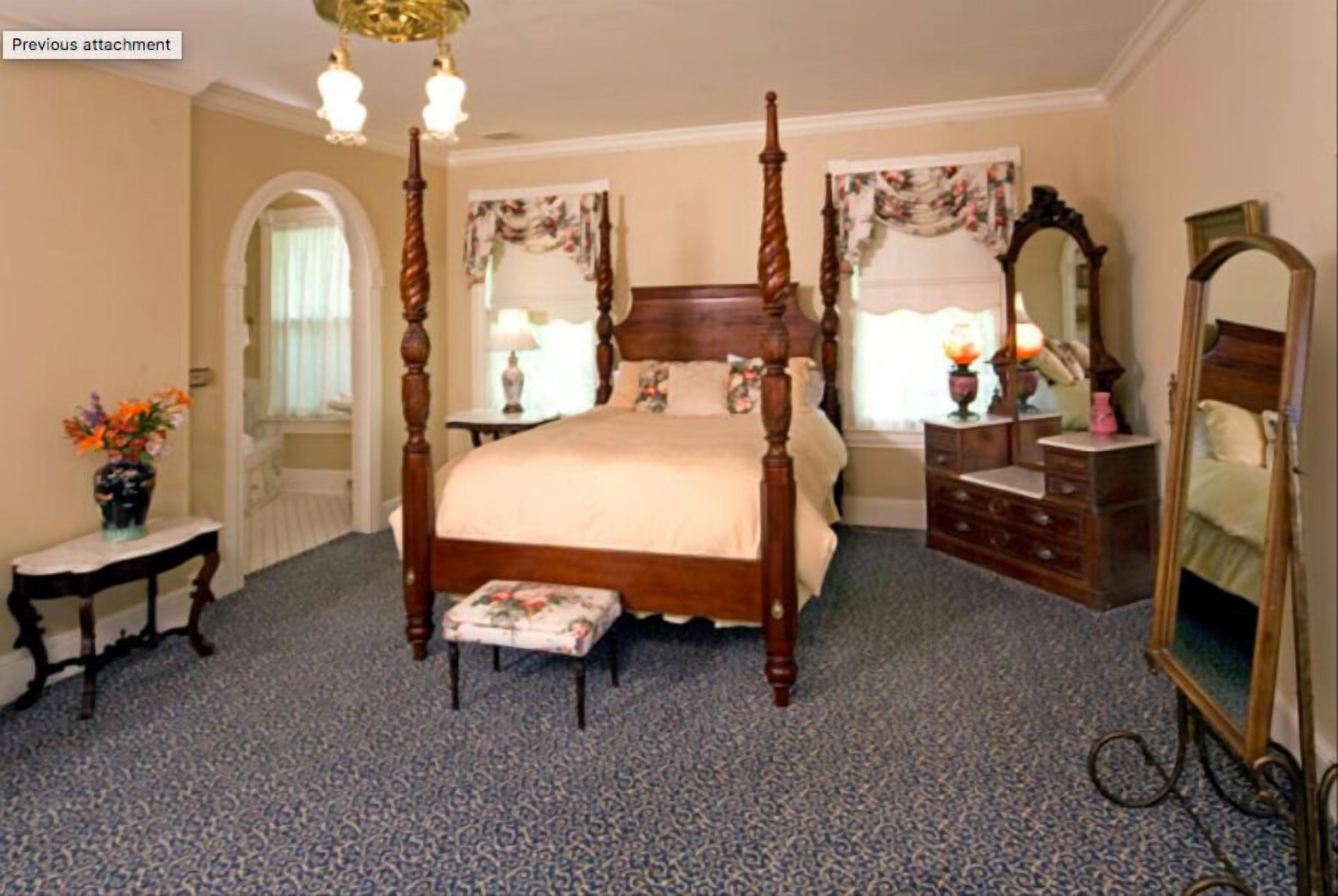 A four-poster bed with a footboard, a dresser, a mirror, and a small table with a vase of flowers.