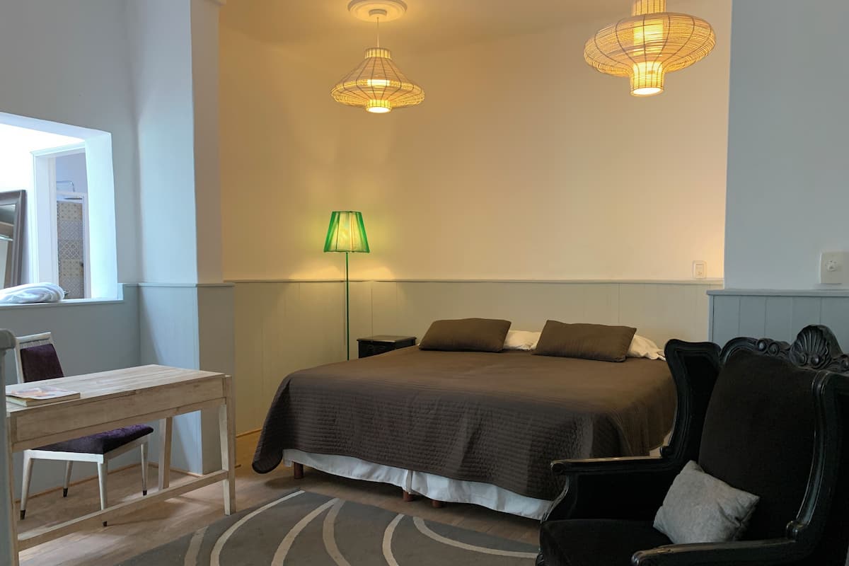 A bedroom with a bed, a desk, a chair, a lamp, and two hanging lights.