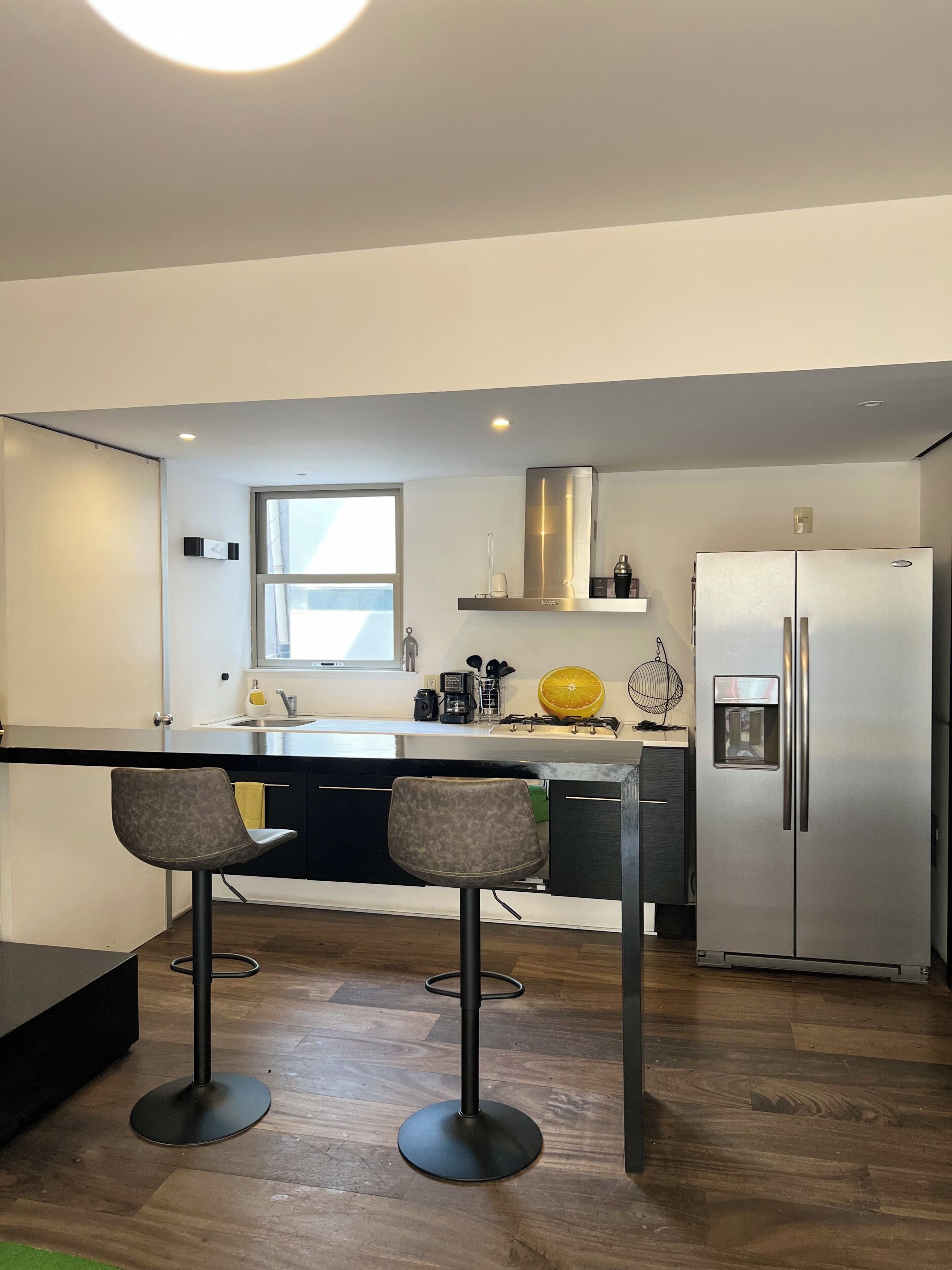 A modern kitchen with a stainless steel refrigerator, a bar stool, and a window.