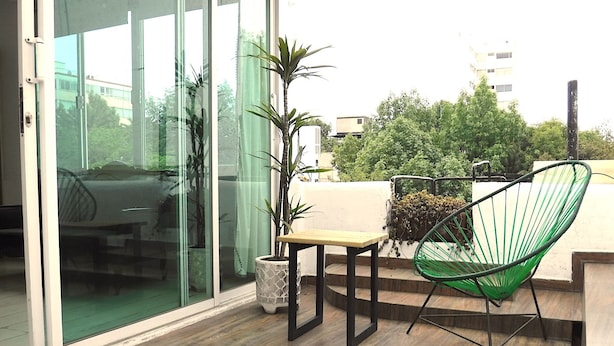 Een balkon met een houten vloer, een groene stoel, een kleine tafel en een bloempot.