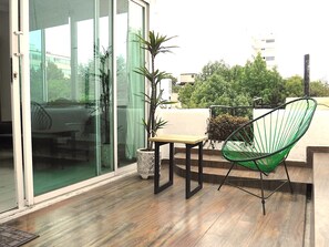 Ein Balkon mit Holzboden, einem grünen Stuhl, einem kleinen Tisch und einem Blumentopf.