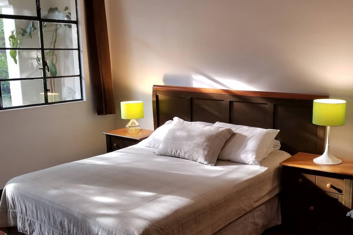 A neatly made bed with a wooden headboard, two bedside tables with lamps, and a window with curtains.